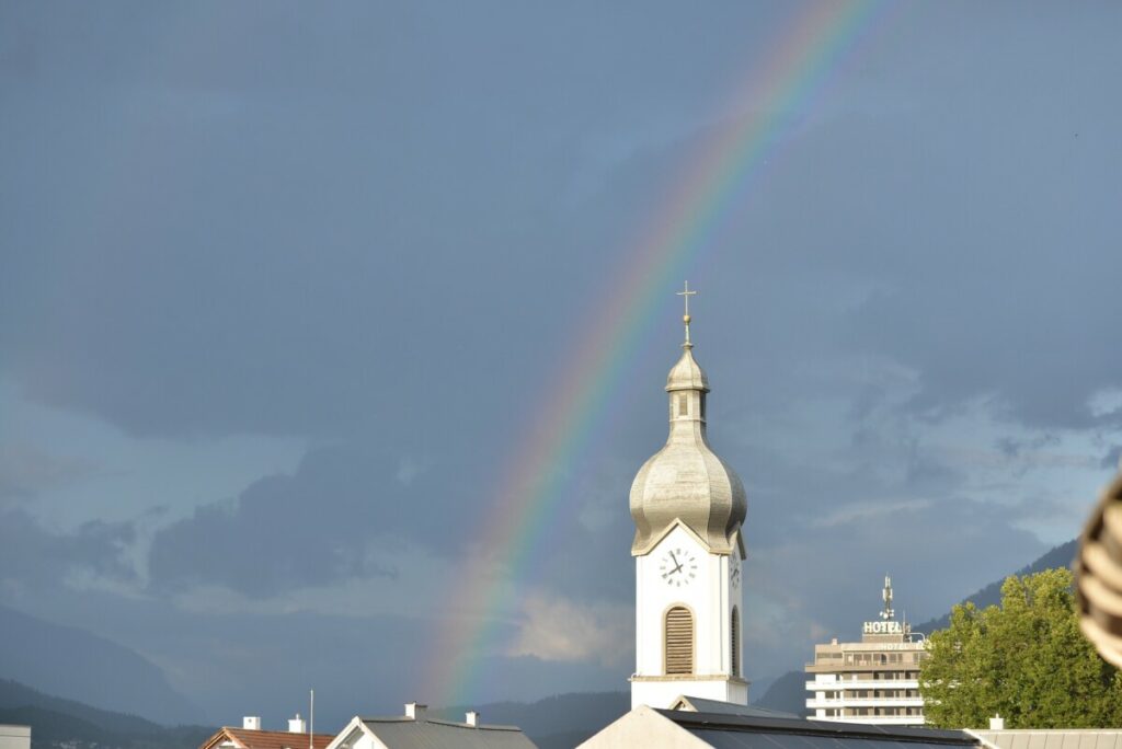 Ein Kirchturm mit einem Regenbogen im Hintergrund.